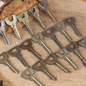 May include: A collection of 16 vintage keys, all with a similar design, laid out on a wooden surface. The keys are made of metal and have a worn, aged look.
