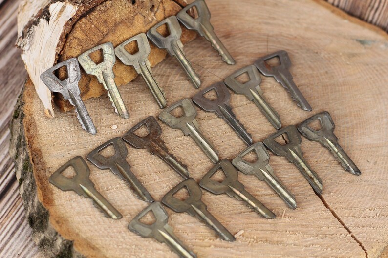 May include: A collection of 16 vintage keys, all with a similar design, laid out on a wooden surface. The keys are made of metal and have a worn, aged look.