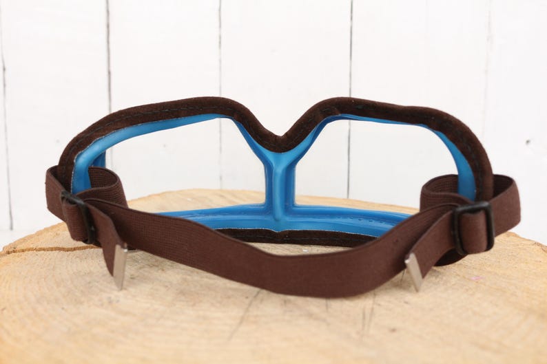 May include: Brown and blue safety goggles with an adjustable strap. The goggles have a clear lens and a soft, padded frame.