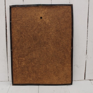 May include: The back of a framed picture with a brown cardboard backing. The frame is black and has a simple design.