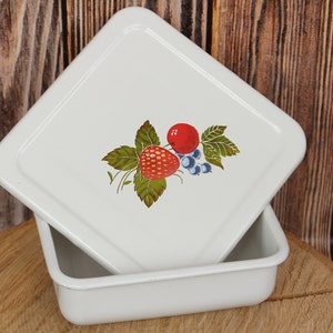 May include: White enamelware baking dish with a lid. The lid features a painted design of strawberries, blueberries, and a red apple.