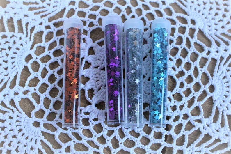 K&ouml;nnte beinhalten: Vier kleine, durchsichtige R&ouml;hrchen gef&uuml;llt mit sternf&ouml;rmigem Glitter. Der Glitter ist in vier Farben: orange, lila, silber und blau.