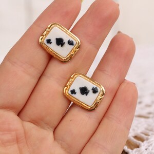May include: A pair of gold-tone cufflinks with a white enamel background and black spade suit symbols.
