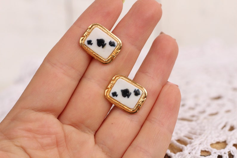 May include: A pair of gold-tone cufflinks with a white enamel background and black spade suit symbols.
