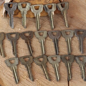 May include: A collection of 18 vintage keys, all made of metal and featuring a similar design. The keys are arranged in three rows of six, with the tips of the keys pointing towards the top of the image. The keys are all a dull silver color, and some have signs of wear and tear.