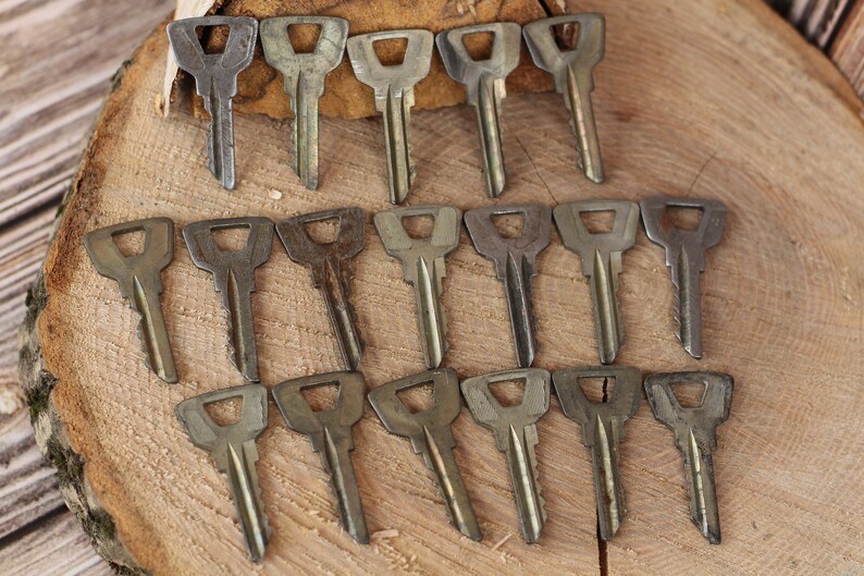 May include: A collection of 18 vintage keys, all made of metal and featuring a similar design. The keys are arranged in three rows of six, with the tips of the keys pointing towards the top of the image. The keys are all a dull silver color, and some have signs of wear and tear.