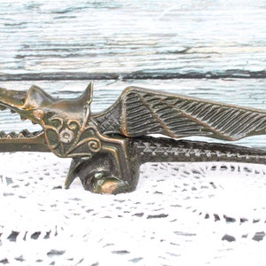 May include: A bronze dragon nutcracker with detailed wings and a textured surface. The nutcracker is open, revealing the jaws that crack nuts.