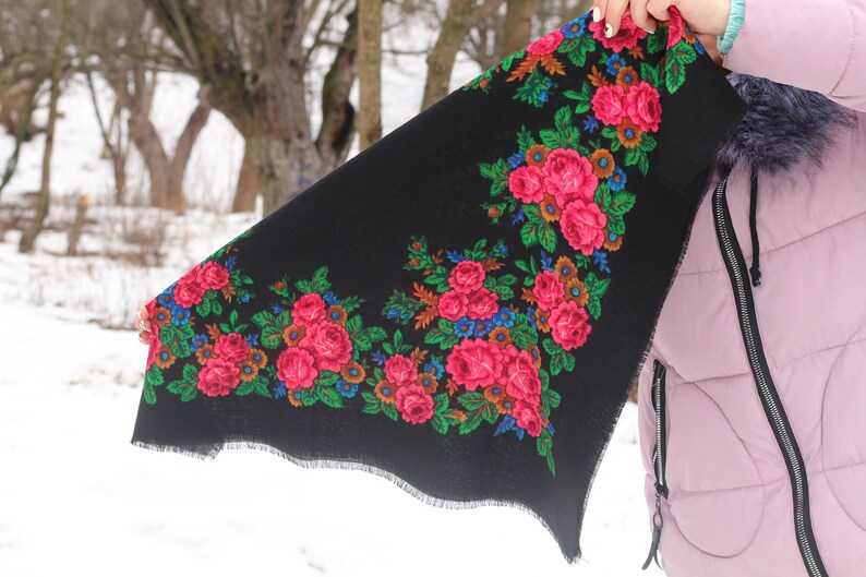 Op de afbeelding: Een zwarte sjaal met een bloemenpatroon met roze, rode, groene en blauwe bloemen. De sjaal heeft een gefranst randje.