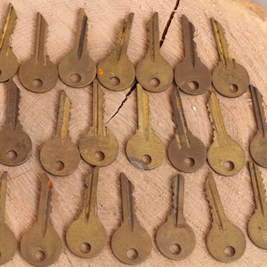 Könnte beinhalten: Eine Sammlung von 24 Vintage-Schlüsseln aus Messing, die in Reihen auf einer Holzoberfläche angeordnet sind. Die Schlüssel sind alle in Größe und Form ähnlich, mit einem runden Kopf und einem geraden Schaft. Sie sind alle in gutem Zustand, mit einer leicht abgenutzten Patina.