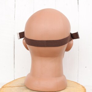 May include: Back view of a brown headband with adjustable straps. The headband is made of a soft, stretchy material and is designed to fit comfortably on the head.