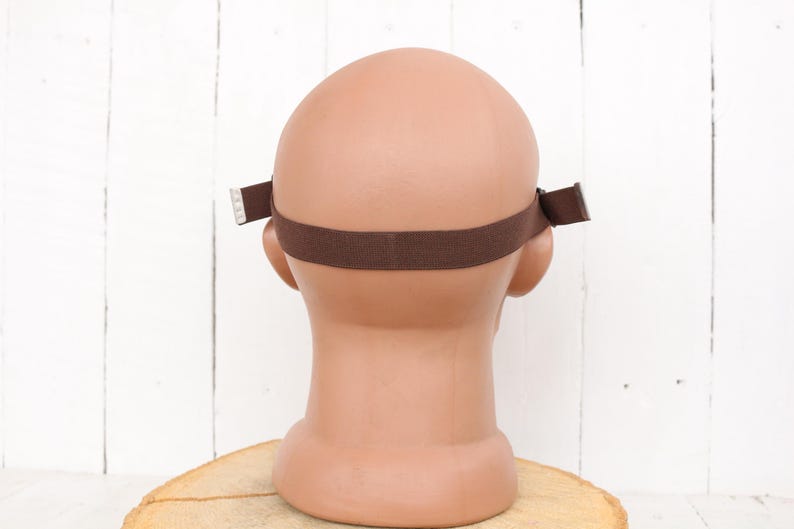 May include: Back view of a brown headband with adjustable straps. The headband is made of a soft, stretchy material and is designed to fit comfortably on the head.