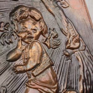 May include: A copper wall plaque with a raised relief design of a young girl with pigtails, wearing a dress and holding a doll. The girl is looking to the right and has a surprised expression on her face. The background is a textured copper surface with a sunburst pattern.
