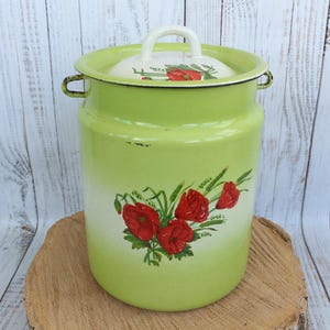 Puede incluir: Una lechera de esmalte verde con tapa blanca y un diseño floral con amapolas rojas. La lechera tiene un borde blanco y una asa blanca.