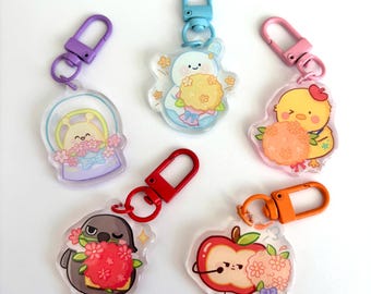 May include: A collection of six clear acrylic keychains with colorful designs. Each keychain features a different cartoon character holding flowers, including a bunny, a chick, a penguin, and an apple. The keychains have various colored clasps.