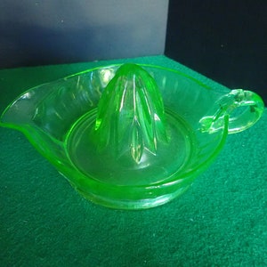 Peut inclure: Un presse-agrumes vintage en verre vert avec un motif cannelé et une poignée. Le presse-agrumes est en verre d'uranium, qui brille sous une lumière noire.