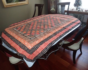 May include: A red and black patterned tablecloth with a geometric design. The tablecloth is laid out on a wooden table with chairs.