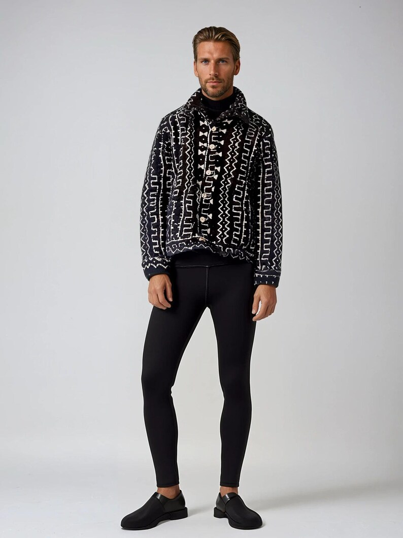 Op de afbeelding: Een zwart-wit gepatroneerd jack met een mock neck shirt en zwarte leggings. De persoon draagt zwarte schoenen.