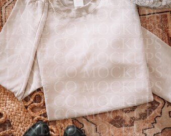 May include: A neutral-toned sweatshirt with a blank label, displayed on a patterned rug. Black leather cowboy boots are at the bottom. A disco ball is in the upper right corner.