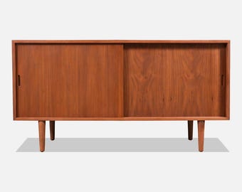 May include: A mid-century modern teak sideboard with two sliding doors and tapered legs. The cabinet is made of solid wood and has a rich brown finish.