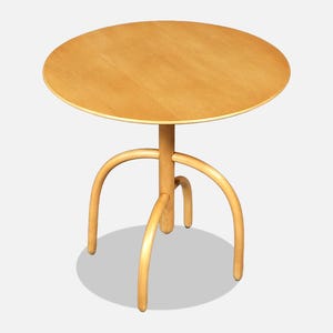 May include: A round light-colored wooden table featuring a smooth circular tabletop surface supported by three curved legs that extend from a central vertical post, creating a stable base structure for this piece of furniture.