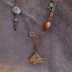 May include: A handcrafted copper necklace featuring turquoise and copper-colored beads and pendants. The necklace has a geometric pendant with a turquoise patina and copper accents, along with a variety of chain styles and textures.