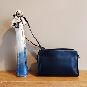 May include: A dark blue leather shoulder bag with a gold clasp. The bag is sitting on a wooden surface.