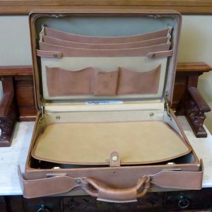 May include: A brown leather briefcase with a flap closure and a handle. The briefcase is open and has multiple compartments and pockets inside. The interior is beige.