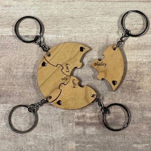 May include: Four wooden puzzle pieces with key rings, each piece has a name engraved on it: Sally, Jen,  Komi, and Hailey.