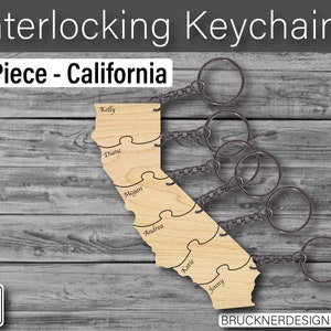 May include: Six wooden keychains shaped like the state of California, each with a different name engraved on it. The keychains are connected by metal rings.
