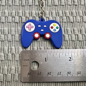 Puede incluir: Llavero de pl&aacute;stico azul en forma de mando de videojuego con un dise&ntilde;o de botones rosa, amarillo, verde y azul. El llavero mide aproximadamente 2,5 cm de largo.