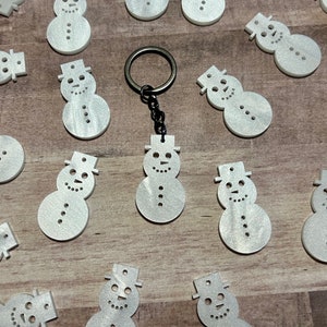 May include: A collection of white, sparkly snowman ornaments with a black key chain featuring a snowman charm.