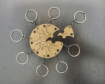 May include: A wooden puzzle keychain set with eight individual pieces, each with a silver keyring. The pieces are engraved with names and heart cutouts. The central piece is a circle with puzzle piece cutouts.