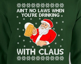 Op de afbeelding: Een donkergroene sweatshirt met een afbeelding van de Kerstman die een bierpul vasthoudt. De tekst "AIN'T NO LAWS WHEN YOU'RE DRINKING WITH CLAUS" staat in het wit. Het ontwerp bevat sneeuwvlokken en decoratieve patronen.