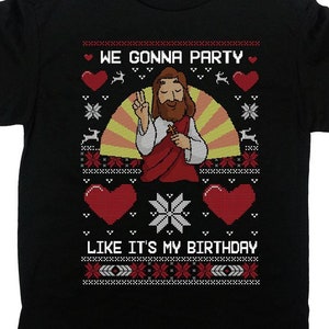 May include: Black t-shirt with a graphic design featuring Jesus giving a peace sign. The text "WE GONNA PARTY" and "LIKE IT'S MY BIRTHDAY" are printed above and below the image, with hearts and snowflakes.