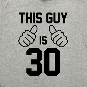 May include: Gray t-shirt with black text that reads "This Guy Is 30" with two thumbs up symbols. The text is in a bold, block font.