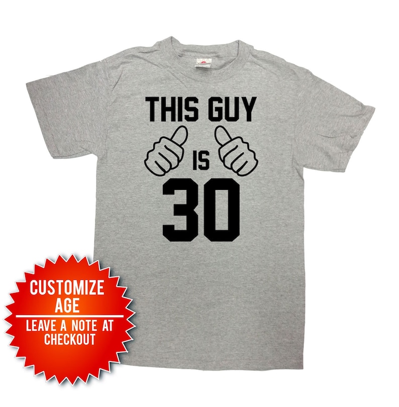 May include: Gray t-shirt with black text that reads "This Guy Is 30" with two thumbs up symbols. The text is in a bold, block font.