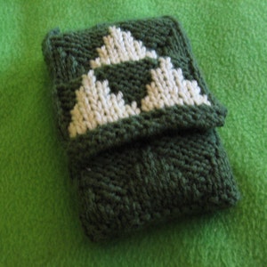 May include: A green knitted phone case with a white triangular design. The case is made of soft yarn and has a textured surface.