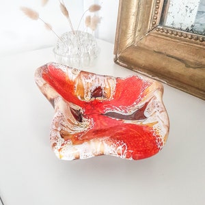May include: A red, orange and white ceramic dish with a wavy, abstract design. The dish is on a white surface.