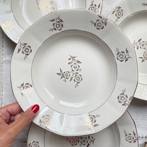 Peut inclure: Ensemble de quatre assiettes en céramique blanche avec un motif floral doré. Les assiettes sont empilées les unes sur les autres.