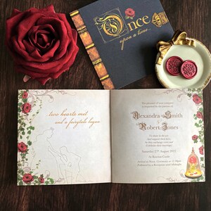 May include: A wedding invitation suite with a fairytale theme. The open invitation features a silhouette of a couple and the text "two hearts met and a fairytale began." A red rose, a book, and a plate with wax seals complete the scene.