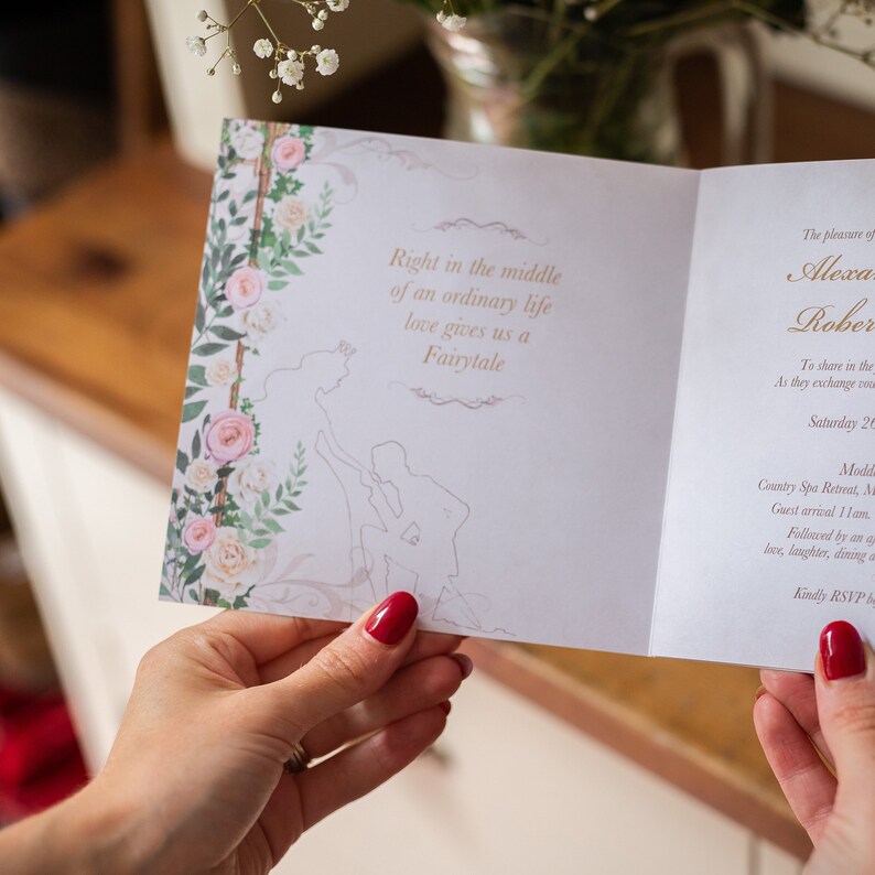 May include: A wedding invitation with floral and fairytale-themed design. The invitation features a floral border with pink and white roses and the text "Right in the middle of an ordinary life love gives us a Fairytale."