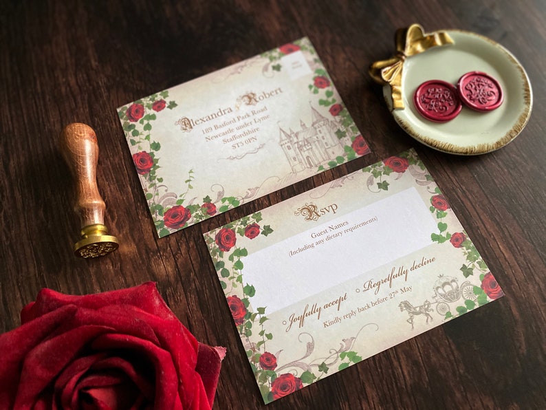 May include: Wedding invitation suite with a vintage aesthetic. The design features a castle illustration, red roses, and ornate script. Includes RSVP cards and a wax seal on a decorative dish. A wooden handled stamp is also present.