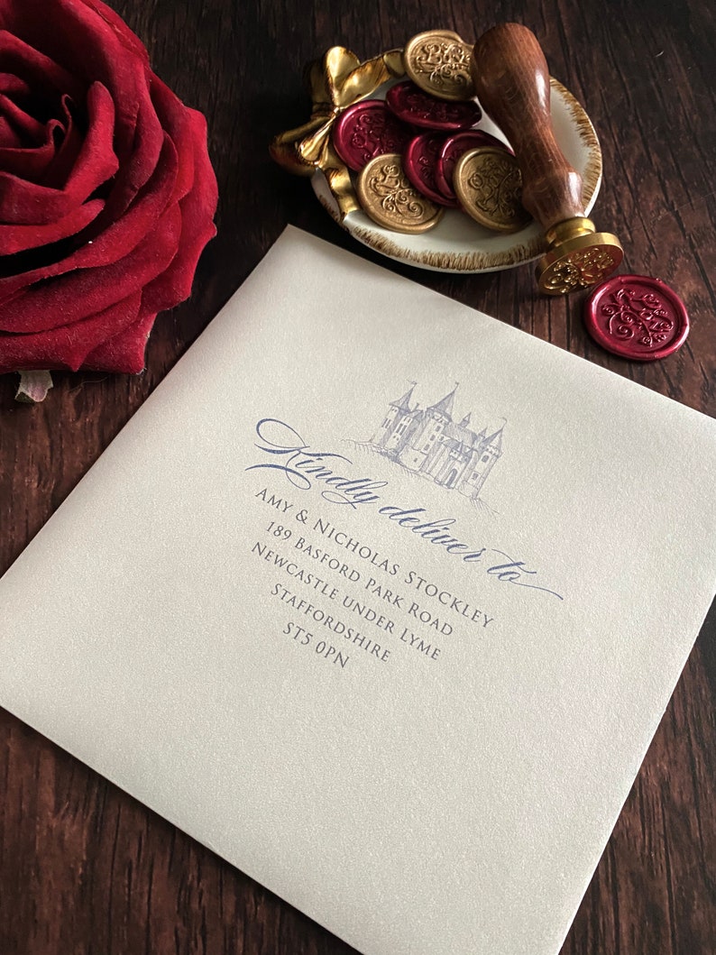 May include: An ivory envelope with a castle illustration and the words "Kindly deliver to" in elegant script. A wooden handled wax stamp and gold and red wax seals are on a decorative dish. A red rose is in the corner.