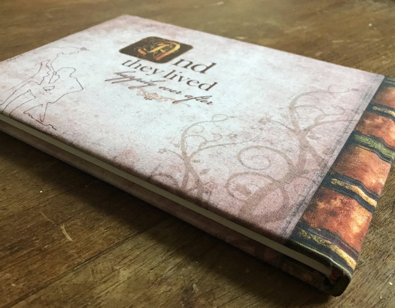 May include: A light brown fabric-covered journal with a decorative spine and the text "And they lived happily ever after." printed on the front cover.