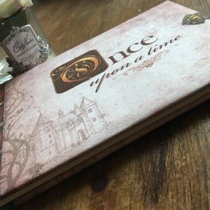 May include: A vintage-style journal with a brown and white cover. The cover features a castle illustration and the text "Once upon a time".