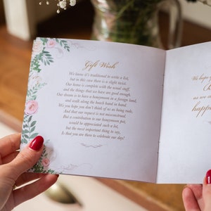 May include: An open wedding card with the words "Gift Wish" in elegant script. The card features floral and leaf border designs in soft pink and green. The text inside is a poem about a honeymoon.