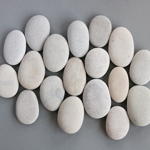May include: A collection of smooth, gray and white stones arranged in a circular pattern on a gray background.