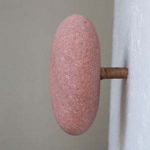 Può includere: Pomello in pietra rosa, di forma ovale e superficie ruvida. È fissato a una parete con un piccolo tassello cilindrico di legno. Elemento decorativo.
