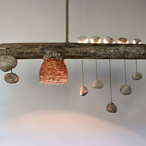 May include: A rustic wooden chandelier with a woven wire shade and multiple hanging stones. The chandelier is made from driftwood and has a natural, organic look.