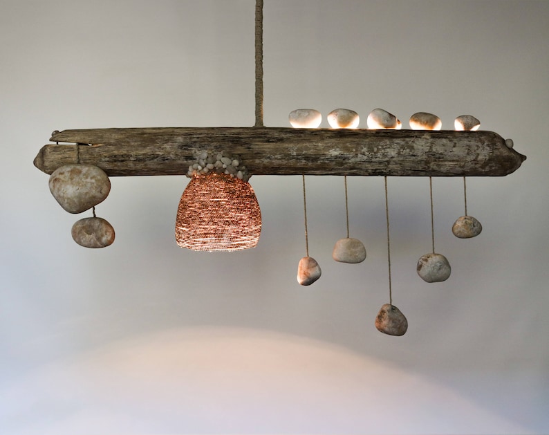 May include: A rustic wooden chandelier with a woven wire shade and multiple hanging stones. The chandelier is made from driftwood and has a natural, organic look.